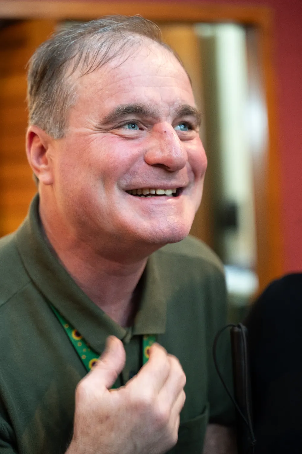 Zezinho Fisioterapeuta em close, sorrindo e olhando para o horizonte, vestindo camisa polo verde e cordão de girassóis.