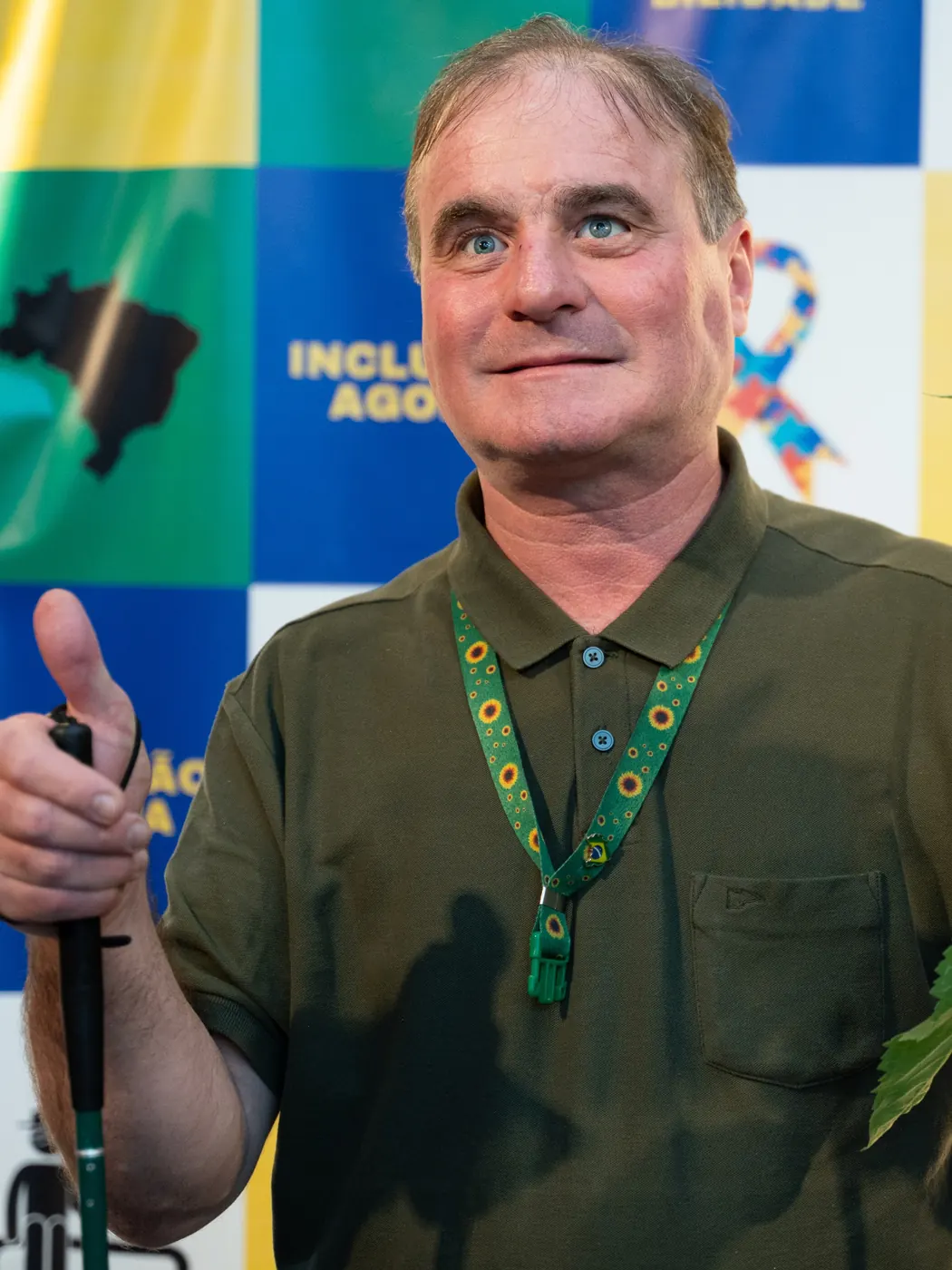 Zezinho Fisioterapeuta sorrindo, com cordão de girassóis, erguendo a bengala branca em ato de pré-campanha.